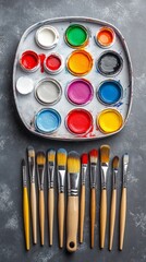 Naklejka premium A vibrant selection of paint colors is organized in a round palette, complemented by various paintbrushes, ready for a creative painting session