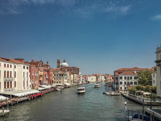 A Sunny Day on the Grand Canal. The canal stretches into the distance, lined with colorful buildings and dotted with boats. The sky is a brilliant blue, adding to the cheerful atmosphere. 