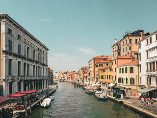 A Venetian Canal Under a Blue Sky. A canal winds its way through the city, lined with colorful buildings and dotted with boats. The sky is a clear blue, adding to the tranquil atmosphere. 