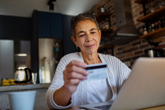 Smiling senior woman making a purchase on laptop with credit card at home