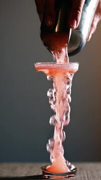 Bartender pouring a Pink Lady cocktail into a coupe glass, creating a dramatic cascading effect.