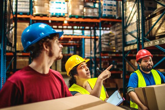 Warehouse workers carrying boxes while supervisor giving instructions in storage facility