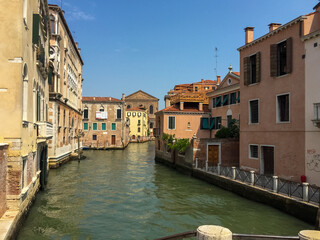 A Narrow Venetian Canal. A narrow canal winds its way through the city, lined with colorful buildings that lean in towards each other. 