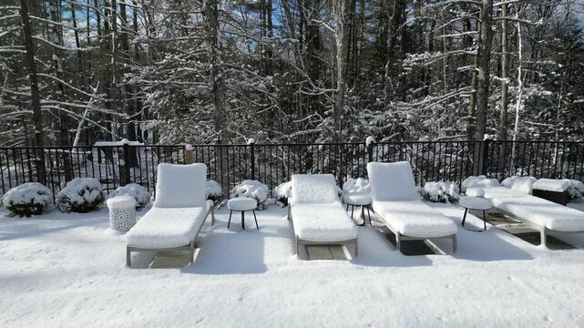 aerial view of snow covered lounge chairs next to closed shuttered swimming pool in winter (back yard patio loungers outdoor furniture) spa bizzard snowy snowfall frozen home countryside drone footage