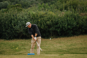A golfer in mid-swing on a grassy golf course, surrounded by lush greenery, focusing on hitting the golf ball with precision.