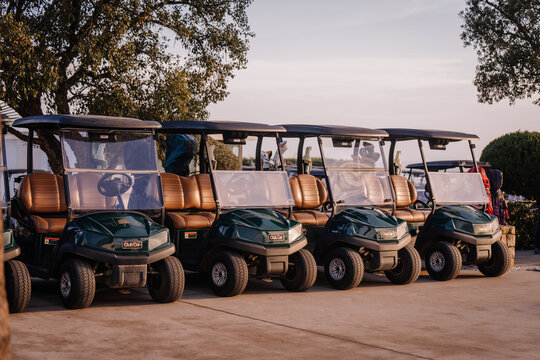 A row of green golf carts with tan seats parked outdoors under the sunlight, ready for use on the golf course.