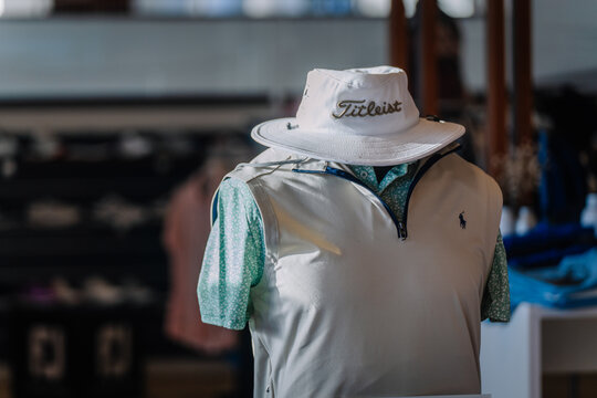 A golf mannequin dressed in a stylish vest, floral shirt, and a &ldquo;Titleist&rdquo; branded hat, showcased in a pro shop with a blurred background.