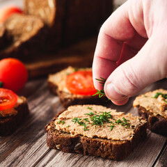 Rustic Pate, man smear on Black Bread with Fresh Herbs and tomatoes