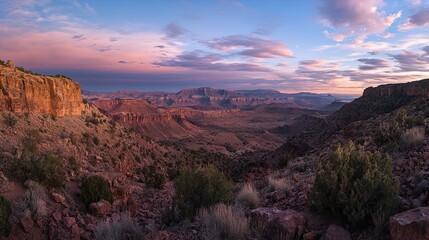 A breathtaking panoramic view of a canyon landscape during twilight, with warm hues of pink and orange in the sky contrasting against the rugged rock formations and rolling hills. The foreground featu
