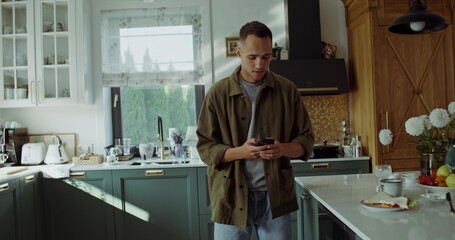 A man uses a mobile phone in the kitchen at home. He looks upset.