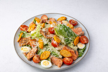 Caesar salad with trout (salmon), cherry tomatoes, croutons, parmesan cheese, quail eggs and romaine lettuce. Traditional American dish. Close-up, selective focus.
