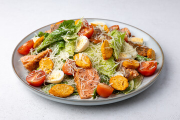 Caesar salad with trout (salmon), cherry tomatoes, croutons, parmesan cheese, quail eggs and romaine lettuce. Traditional American dish. Close-up, selective focus.