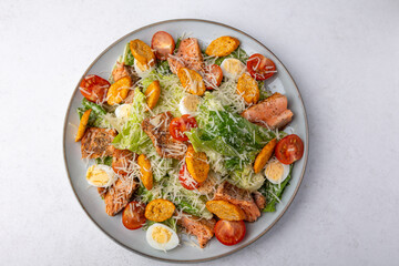Caesar salad with trout (salmon), cherry tomatoes, croutons, parmesan cheese, quail eggs and romaine lettuce. Traditional American dish. Close-up, selective focus.