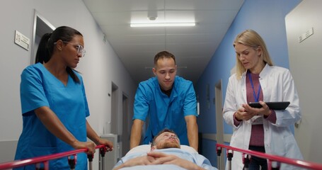 Medical workers carry a patient on a gurney along the hospital corridor. They are smiling and talking to a man