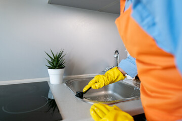 A housewife cleans the sink with a brush; cleaning products help eliminate unpleasant odors like...