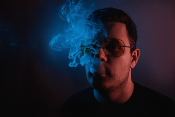 Neon ambiance surrounds man with glasses as he enjoys smooth smoke in a chill lounge atmosphere