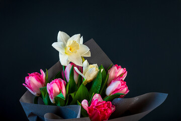 Bright spring bouquet of white daffodils and pink tulips, wrapped in dark paper, on a black background. Water drops on the petals add freshness and tenderness. Ideal for flower advertising and holiday