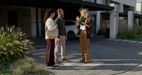 The realtor shows the booklet to customers standing near the townhouse for sale