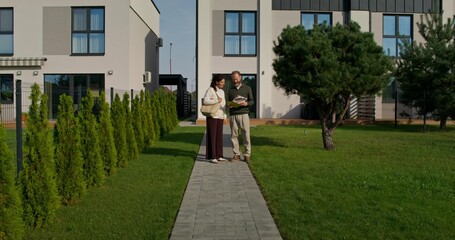 Obraz premium A man and a woman study the design project of a house while walking in the backyard. Making a decision about buying a property