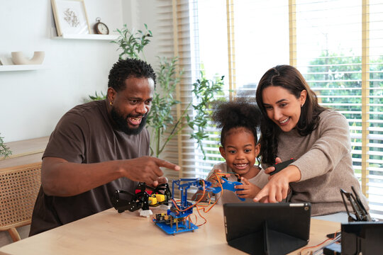 Happy african american father, mother, and daughter enjoying time together building a robotic arm at home, engaging in a fun and educational stem activity for kids
