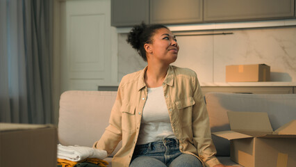 African American ethnic woman happy girl homeowner renter unpacking box on sofa moving in new home cheerful smiling female customer unpack parcel order clothes online shopping delivery relocation day