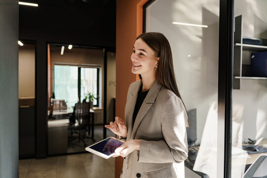 Young professional woman engages in conversation while holding a tablet in a modern office setting - Powered by Adobe