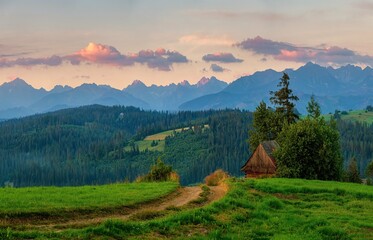 Mountain landscape at sunrise with a dirt road and an old wooden house on a mountain meadow, mountain peaks in the background. Tatra mountain landscape in Poland