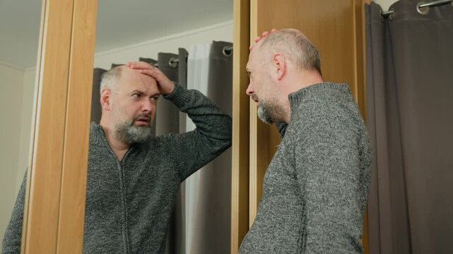 Upset man crying over hair loss, struggling with balding. Emotional reaction to thinning hair as he touches scalp. Hair loss problem causing distress and frustration