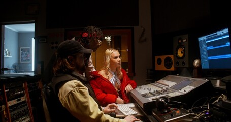 The sound engineer talks to the musicians after recording the song in the studio. They are sitting in front of the equipment in the control room