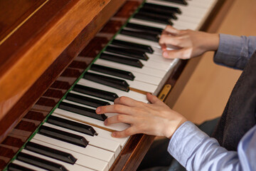 Fototapeta premium Close up of boy's hands playing piano. Child has piano lesson. Development of musical abilities, piano fingering. Top view. Selective focus.