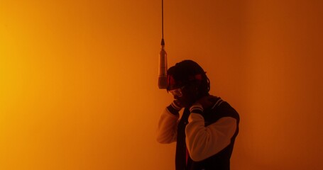 A modern man raps into a microphone. Orange light, video clip recording