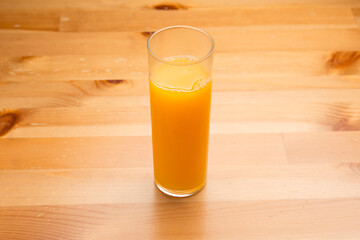 Glass of fresh squeezed orange juice resting on a light wooden table