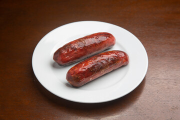 Grilled sausages sizzling on crisp white plate, nestled atop rustic wooden surface, presenting tempting meal ready for enjoyment