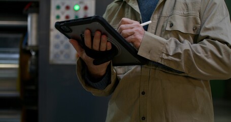 A man uses a tablet while working at a factory. Close-up of his hands, an unrecognizable person