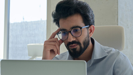 Pensive ethnic man Arabian Indian muslim businessman male employer corporate CEO at office with computer laptop business work planning thinking solve issue think ponder idea problem solution look away