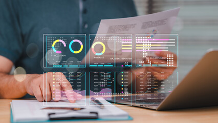 A man is looking at a computer screen with a lot of graphs and numbers. He is holding a piece of paper in front of him