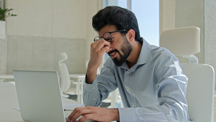Arabian Indian man tired exhausted worker manager working laptop computer sick businessman rubbing dry itchy eyes male business employer overwork in office take off glasses feel headache bad vision