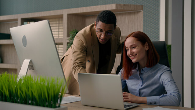 African American man boss mentor coach businessman teaching new employee at workplace team leader help advice Caucasian woman intern with laptop computer online project in office corporate teamwork 