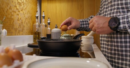 A man breaks eggs into a frying pan. Cooking breakfast at home. Close-up of his hand, an unrecognizable person