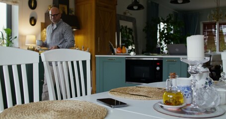 The man cooks his own food. He carries a full plate and a cup of coffee to the table. Daylight