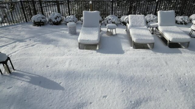 aerial view of snow covered lounge chairs next to closed shuttered swimming pool in winter (back yard patio loungers outdoor furniture) spa bizzard snowy snowfall frozen home countryside drone footage