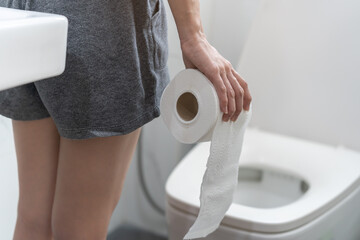 Stomach ache, sick asian young woman holding stomach pain and holding tissue paper roll in...