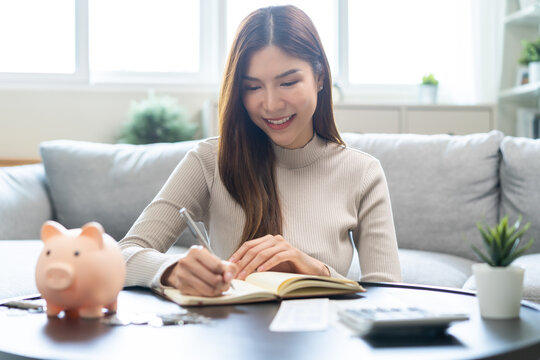Saving money wealth concept, asian young business woman hand write management budget for saving cost, cash finance planning to spend enough money on her income for save money, payment tax, investing.