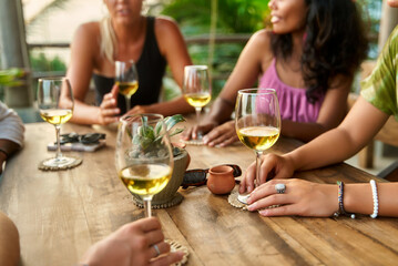 Diverse women enjoy wine tasting, sharing laughter and stories, at a cozy restaurant. Relaxing at a rustic table, sunlight streams in. Perfect for lifestyle, friendship, relaxation, social events.