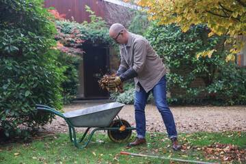 Mature man cleaning dry leaves in garden at autumn