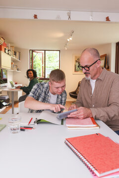 Father helping adult son with homework, mother working in background