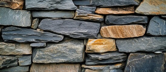 Textured stone wall composed of various sized slate stones in gray and brown tones suitable for background design and architectural applications