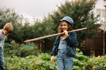 Cute girl and teenager boy working in a garden with rake and shovel. Countryside farm.