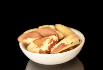Several Brazil nuts on a white ceramic saucer, close-up, isolated on a black background.