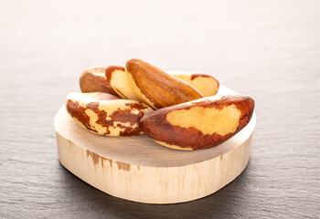 Several Brazil nuts with a wooden tray on a slate stone, close-up.